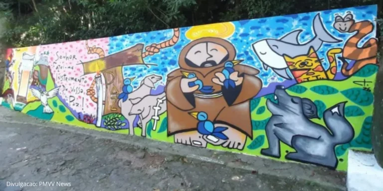 Mural colorido pintado para a Festa da Penha 2026 com ilustrações religiosas e elementos da natureza, incluindo São Francisco, animais e símbolos de paz, em parede externa cercada por vegetação.