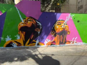 Mural de grafite com crianças cuspindo jatos de água, retratando o costume de banho de mar na “maré” da comunidade de Caratoíra, em Vitória-ES, criado no projeto Vizinho da Arte com apoio da Politintas.