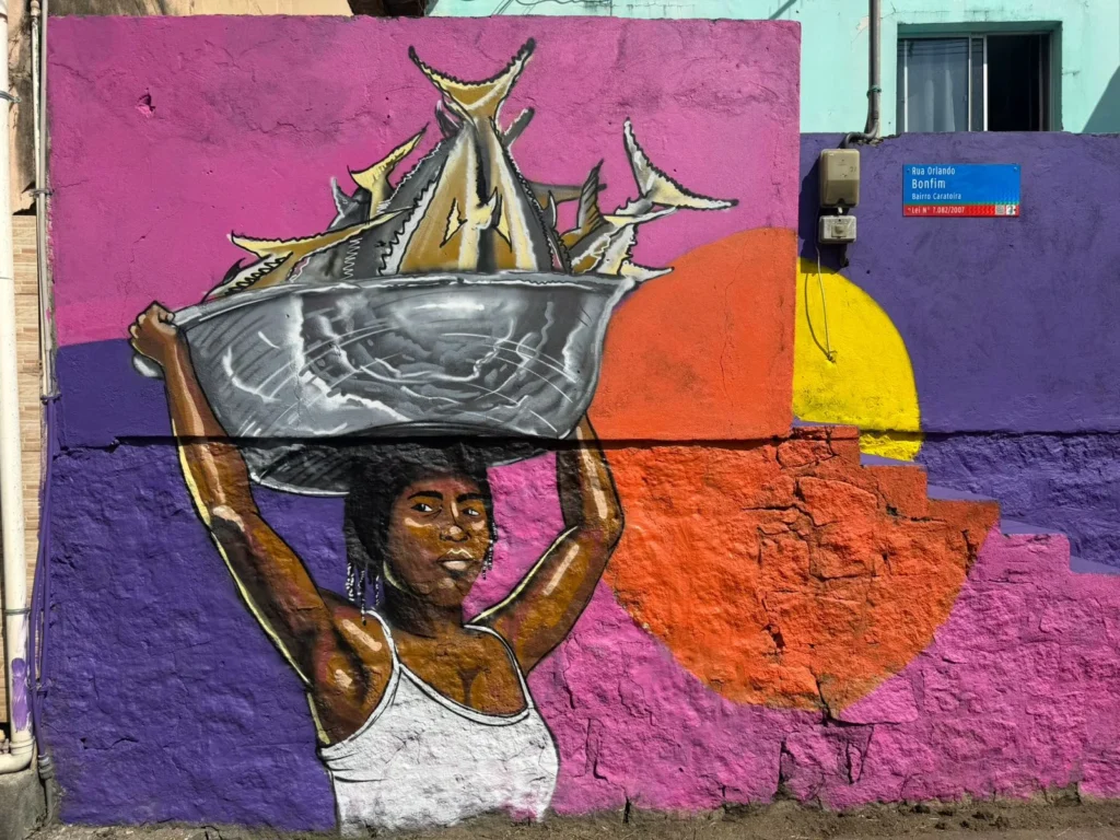 Mural de grafite retratando mulher carregando bacia com peixes sobre a cabeça, inspirado na cultura e no cotidiano popular de Caratoíra, em Vitória-ES, no projeto Vizinho da Arte.